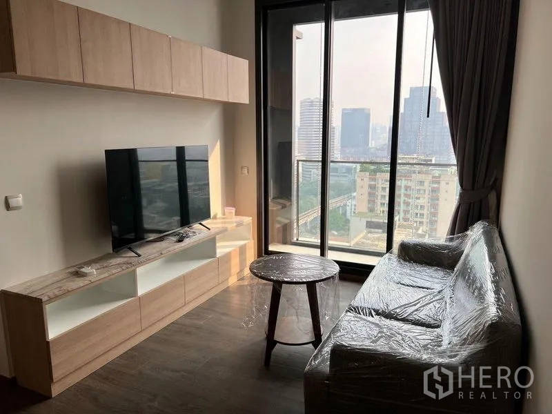 Condominium for rent in Ratchathewi, Bangkok - Compact living room with TV unit, sofa and balcony access with city views.