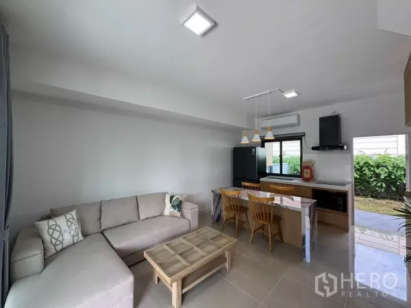 Townhouse for rent in Bang Phli, Samut Prakan - Open-plan living, dining and kitchen with L-shaped sofa, island and garden outlook.