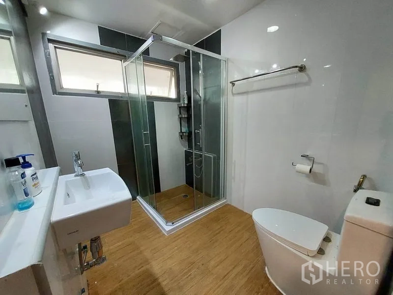 Condominium for rent or sale in Khlong Toei, Bangkok - Modern bathroom with glass shower enclosure, window and white fixtures.