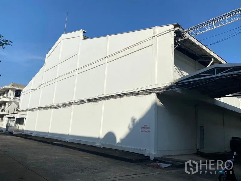 Warehouse for rent in Mueang Samut Prakan, Samut Prakan - White warehouse exterior facade with sloped roof under a clear blue sky.
