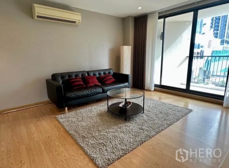 คอนโด ให้เช่าในWatthana, Bangkok - ห้องนั่งเล่นโซฟาหนังสีดำ พรม และประตูกระจกบานเลื่อนออกระเบียง