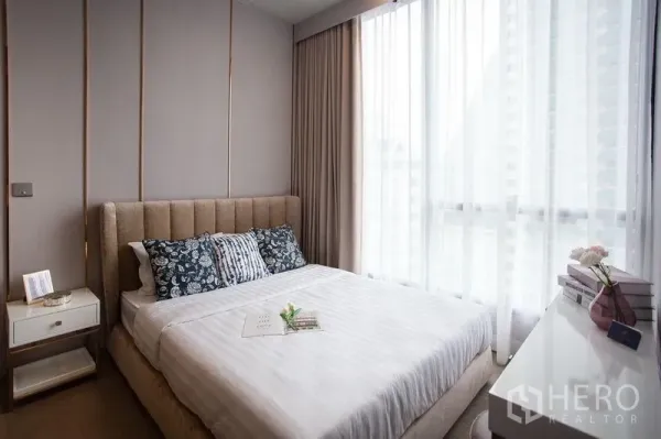 Condominium for rent in Watthana, Bangkok - Bright bedroom with upholstered bed, bedside table and large window with sheer drapes.