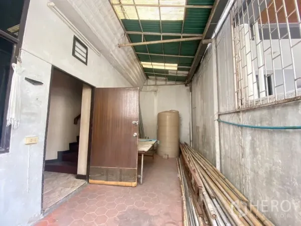 Retail Space for rent in Watthana, Bangkok - Covered rear service area with tiled floor, wooden door and stored pipes along the wall.