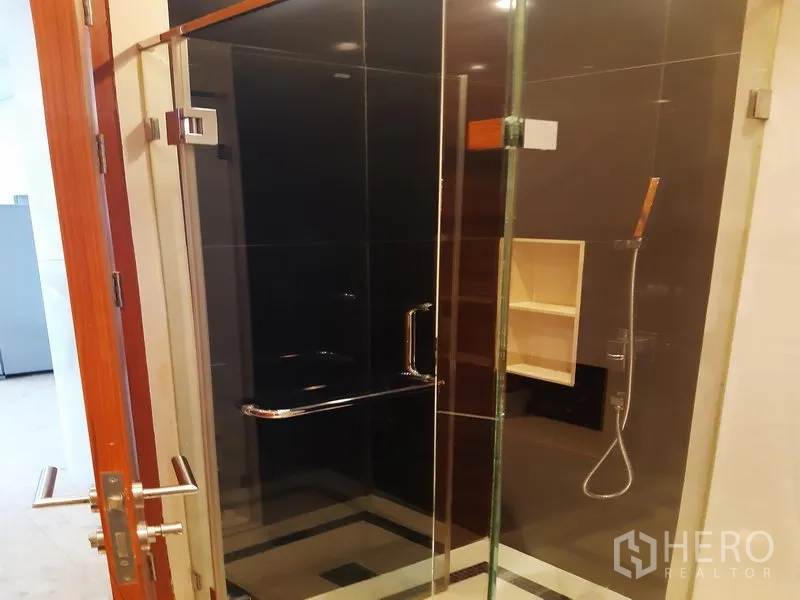 Condominium for rent in Khlong Toei, Bangkok - Glass-enclosed shower with dark tile walls and handheld shower head.