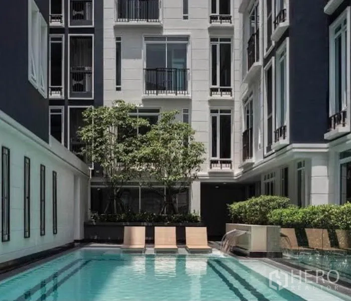 Condominium for rent in Sathon, Bangkok - Condominium outdoor swimming pool with sun loungers, greenery and low-rise facade.