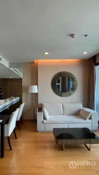Condominium for rent or sale in Bang Rak, Bangkok - Open-plan living area with sofa, dining chairs, wood floors and warm recessed lighting beside the kitchen peninsula.