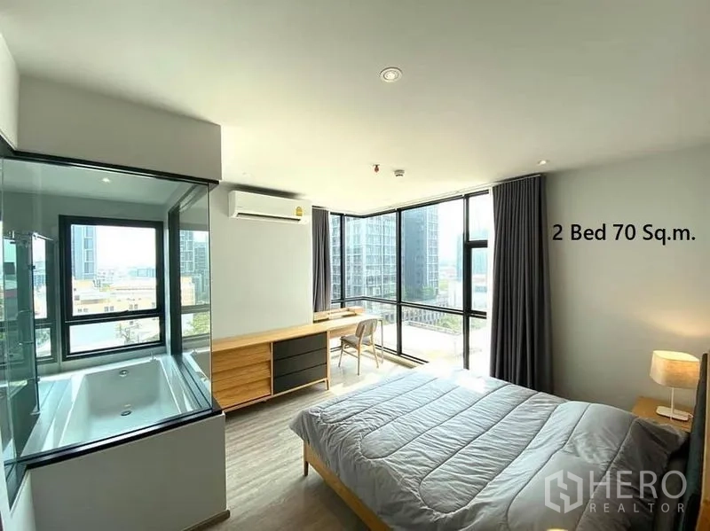 公寓 出租在Watthana, Bangkok - 转角主卧，环幕窗景、内置书桌与玻璃围合的浴缸。