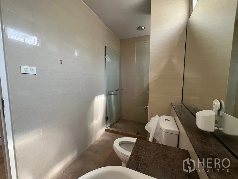 Townhouse for rent in Din Daeng, Bangkok - Modern bathroom with long vanity, mirror, toilet and glass-enclosed shower.