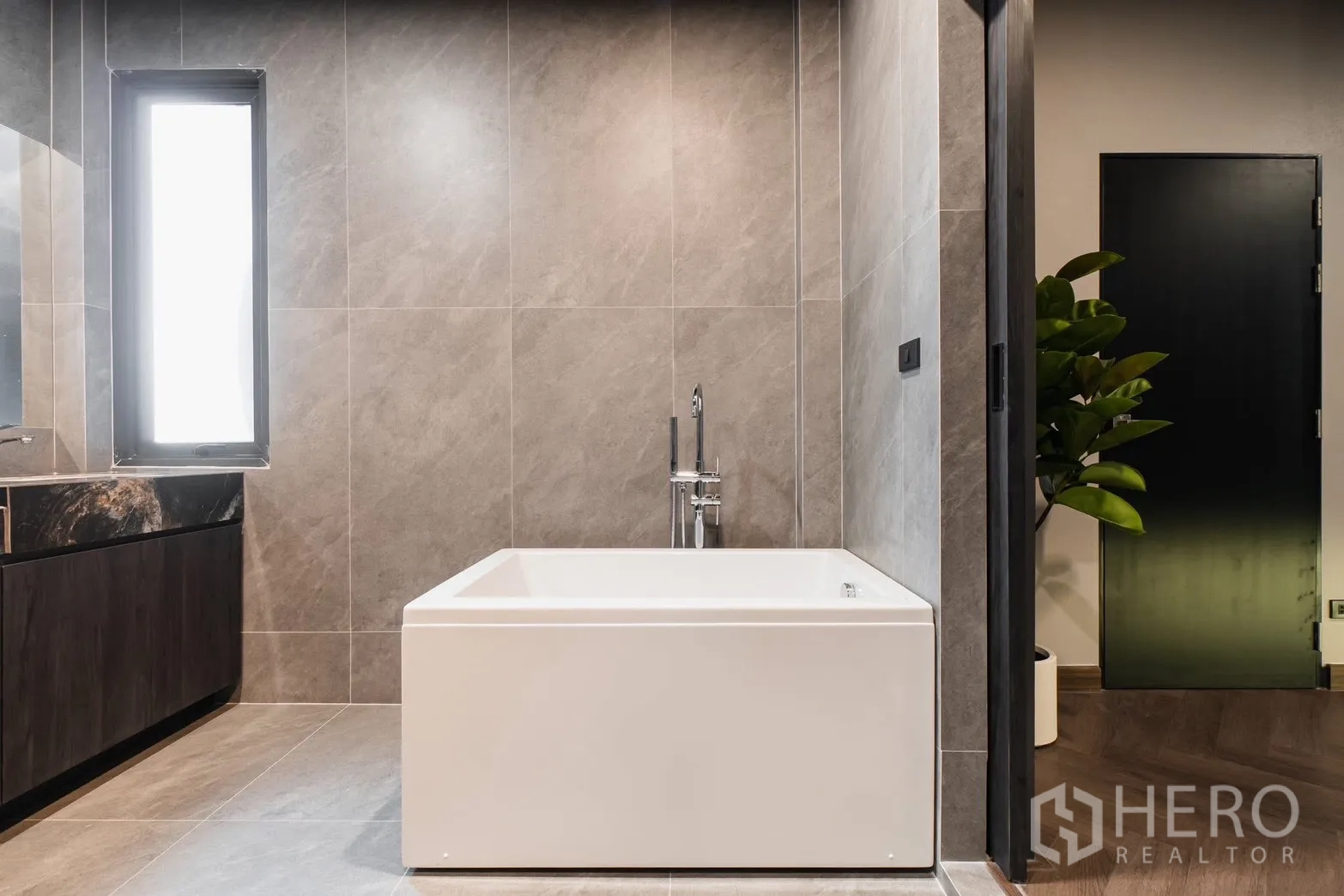 Detached House for rent or sale in Prawet, Bangkok - Bathtub corner beside window in large gray-tiled bathroom