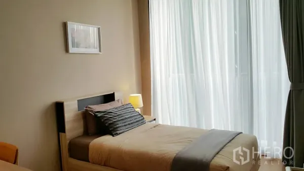 Condominium for rent or sale in Khlong Toei, Bangkok - Second bedroom with a single bed beside sheer floor-to-ceiling curtains and warm lighting.