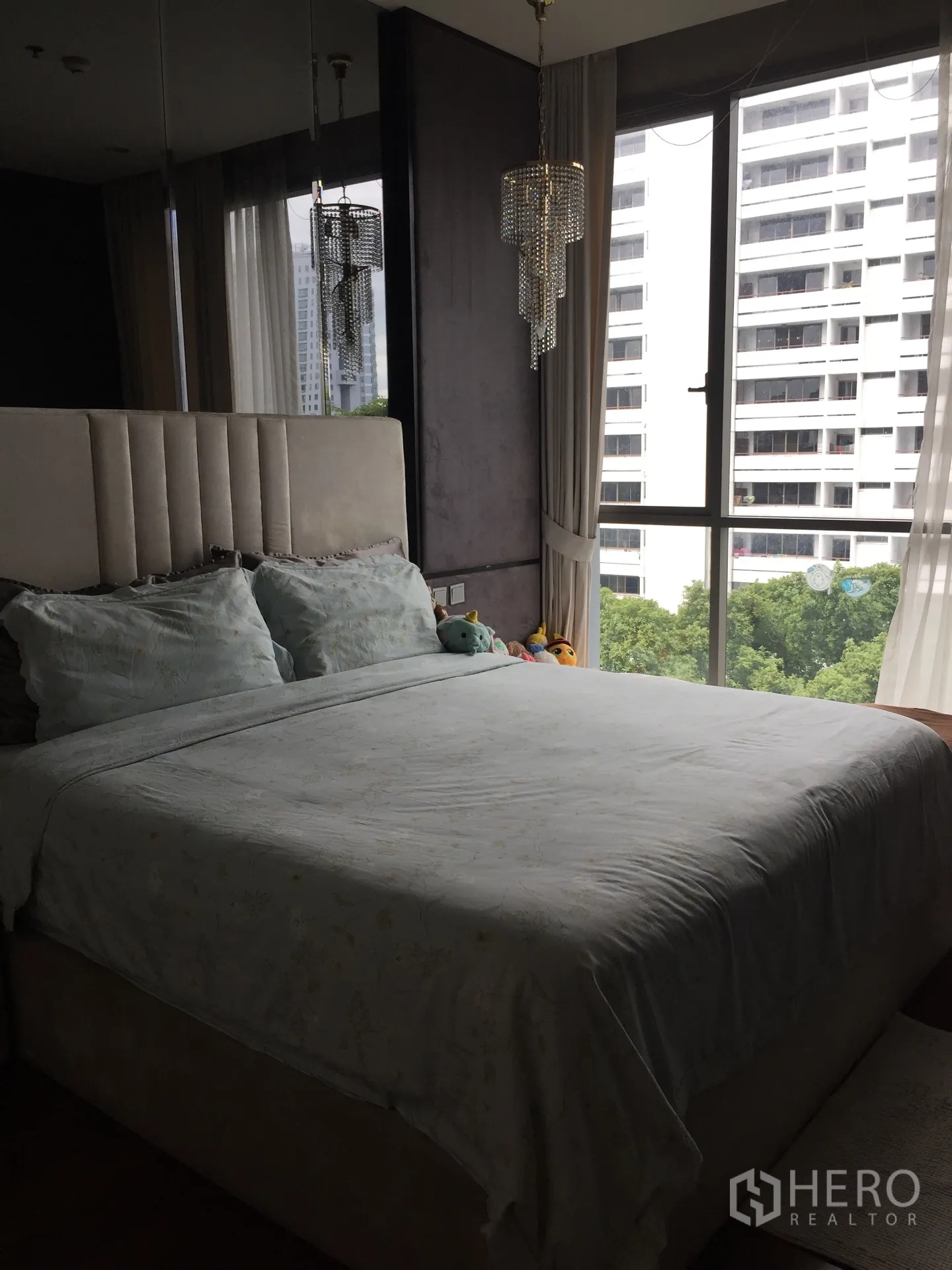 คอนโด ขายในWatthana, Bangkok - ห้องนอนใหญ่มีหัวเตียงบุผ้า โคมระย้า และหน้าต่างมุมกว้างมองเห็นต้นไม้และตึกสูง