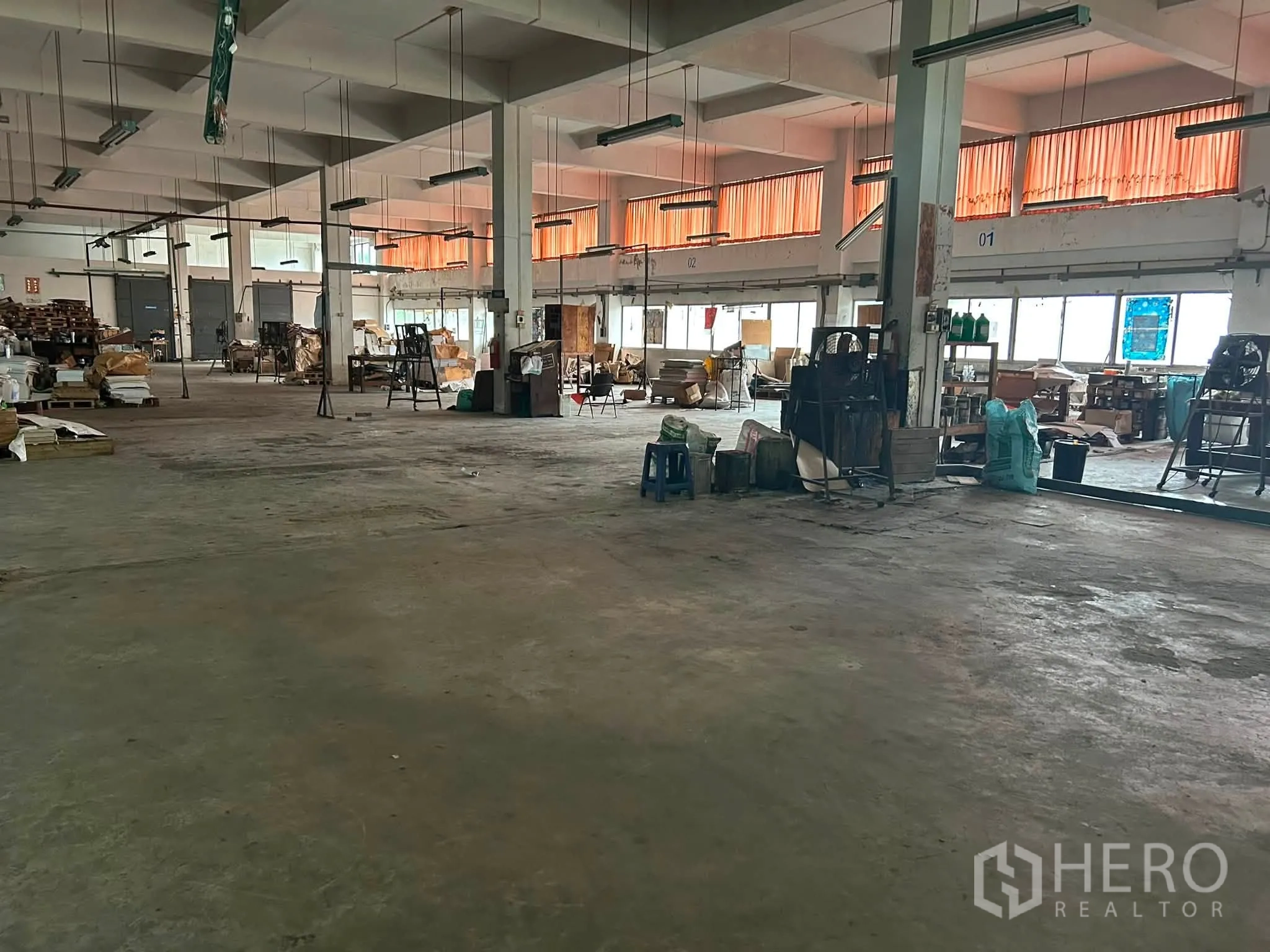 Warehouse for rent in Phra Khanong, Bangkok - Open warehouse interior with concrete floor, columns, windows, and suspended lighting across the hall.