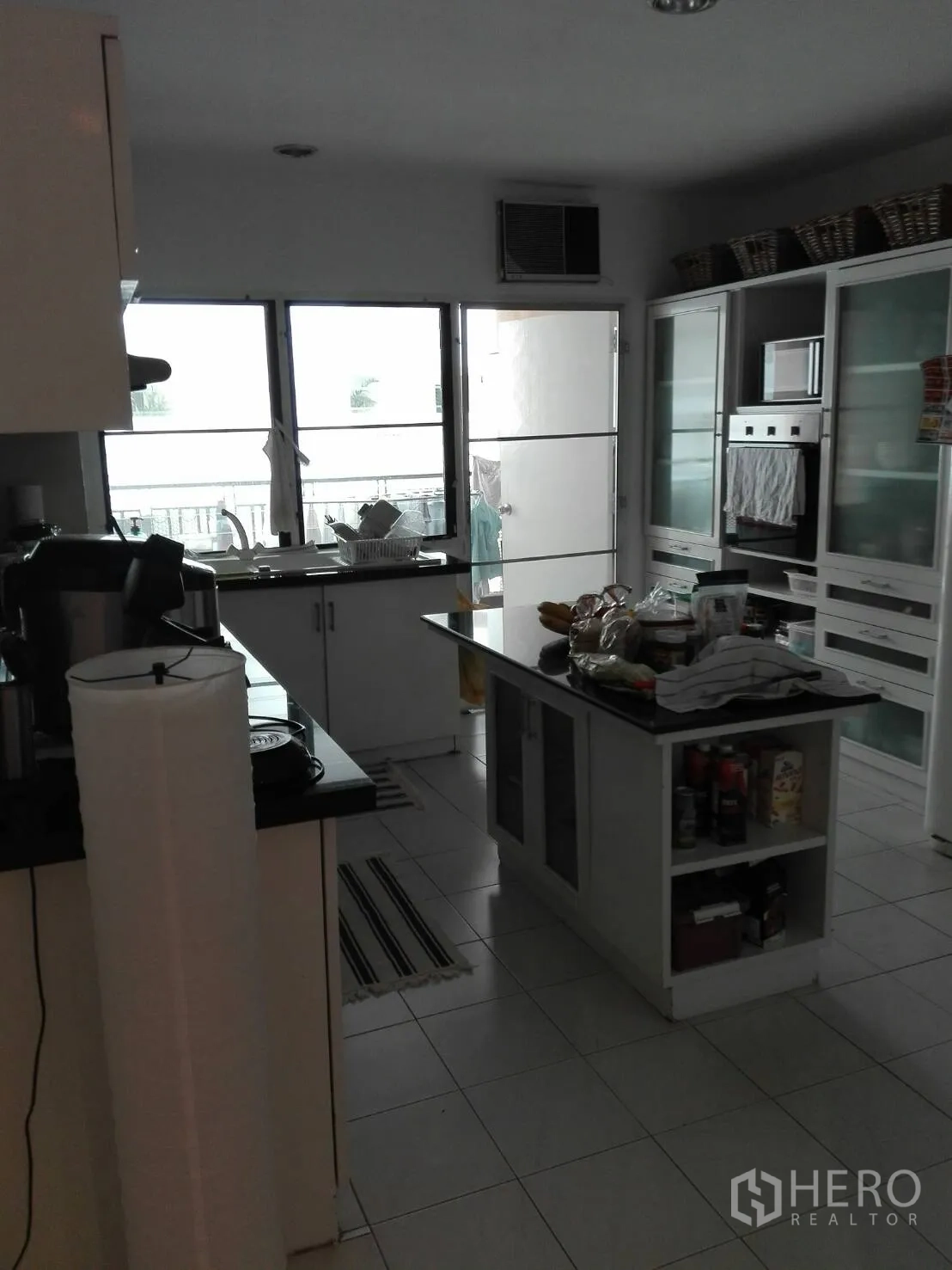 Condominium for rent in Khlong Toei, Bangkok - Fitted kitchen with center island, stone countertops, white cabinetry and a built-in oven.