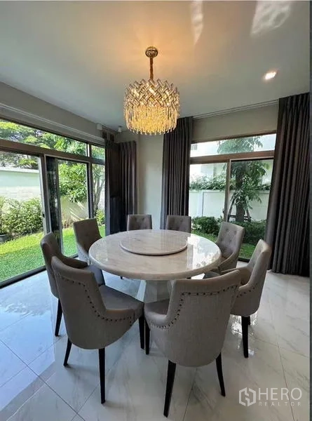 Detached House for rent in Lat Krabang, Bangkok - Dining room with round table for eight under a crystal chandelier and garden views.