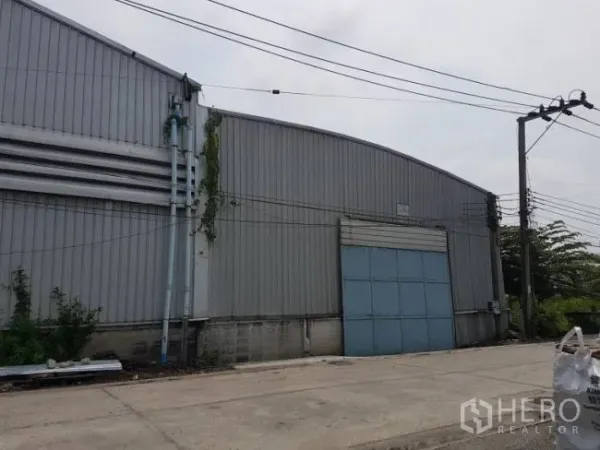 Factory for rent or sale in Bang Phli, Samut Prakan - Side elevation of the warehouse with arched roof and a large blue roller-shutter loading door.