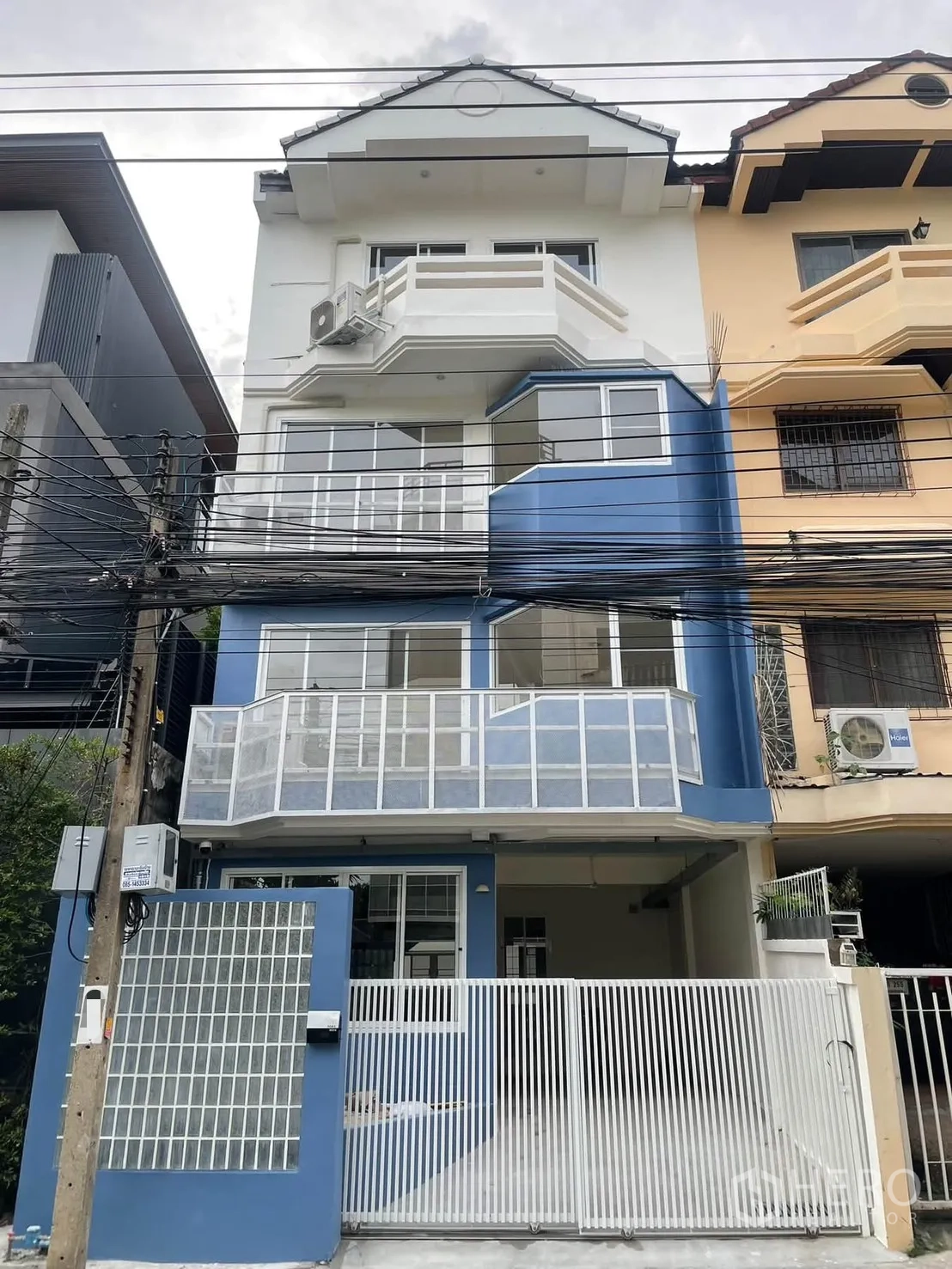 Townhouse for rent in Huai Khwang, Bangkok - Multi-level townhouse exterior with balconies, blue-and-white facade, and gated carport.