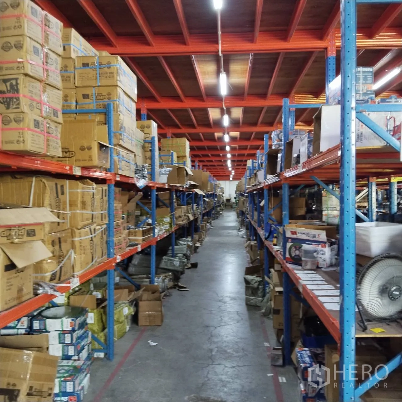 Warehouse for rent in Bang Khun Thian, Bangkok - Long aisle between shelving units under mezzanine level lighting.