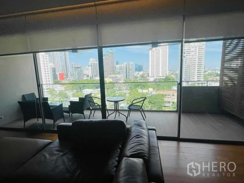公寓 出租或出售在Watthana, Bangkok - 覆盖式阳台配座椅，通过落地玻璃欣赏城市天际线景观。