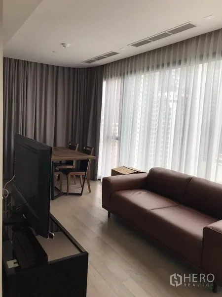 Condominium for rent in Watthana, Bangkok - Open-plan lounge with dining set by large windows, grey drapes, leather sofa and media unit.