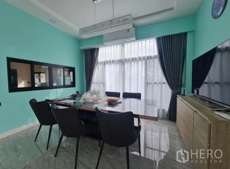 Detached House for sale in Sai Mai, Bangkok - Dining room from another angle showing a large table, turquoise walls, and blackout curtains.