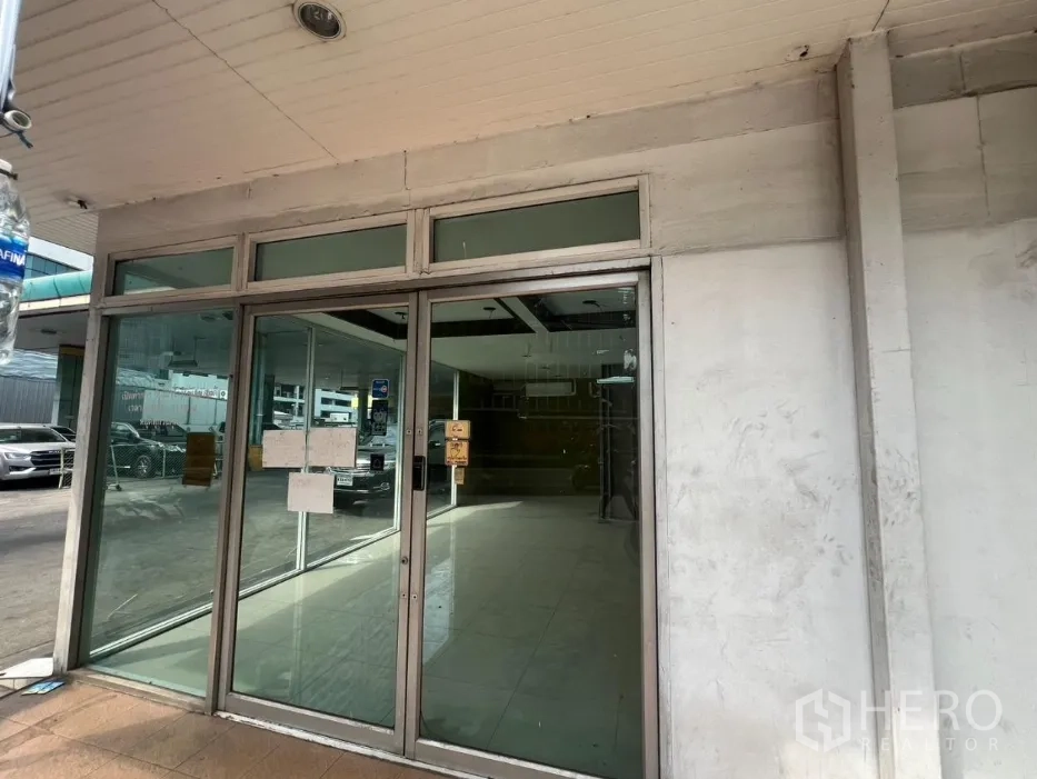 零售空间 出租在Khlong Toei, Bangkok - 玻璃滑门店面入口与瓷砖地面，外侧为停车区。
