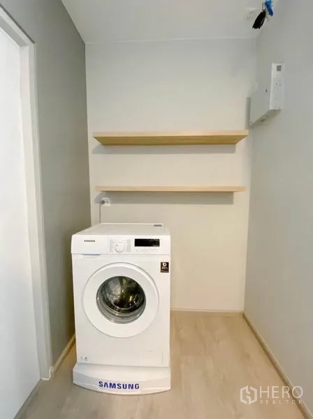 Detached House for rent in Prawet, Bangkok - Compact laundry nook with front-loading washing machine and wall shelves.
