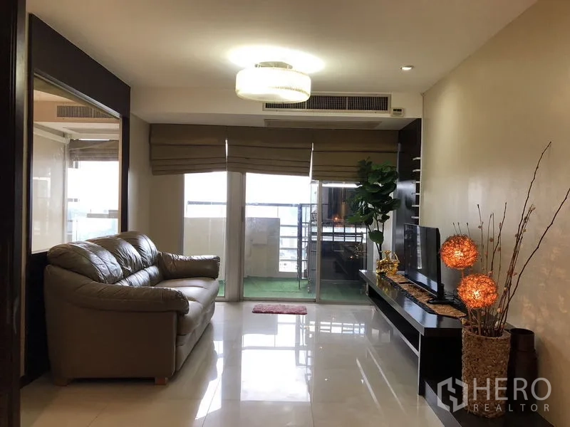 Condominium for rent in Khlong Toei, Bangkok - Bright living room with leather sofa, TV console and sliding doors to the balcony.