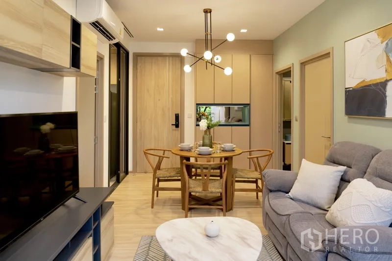 Condominium for rent or sale in Watthana, Bangkok - Open-plan living and dining area with round table and modern chandelier.