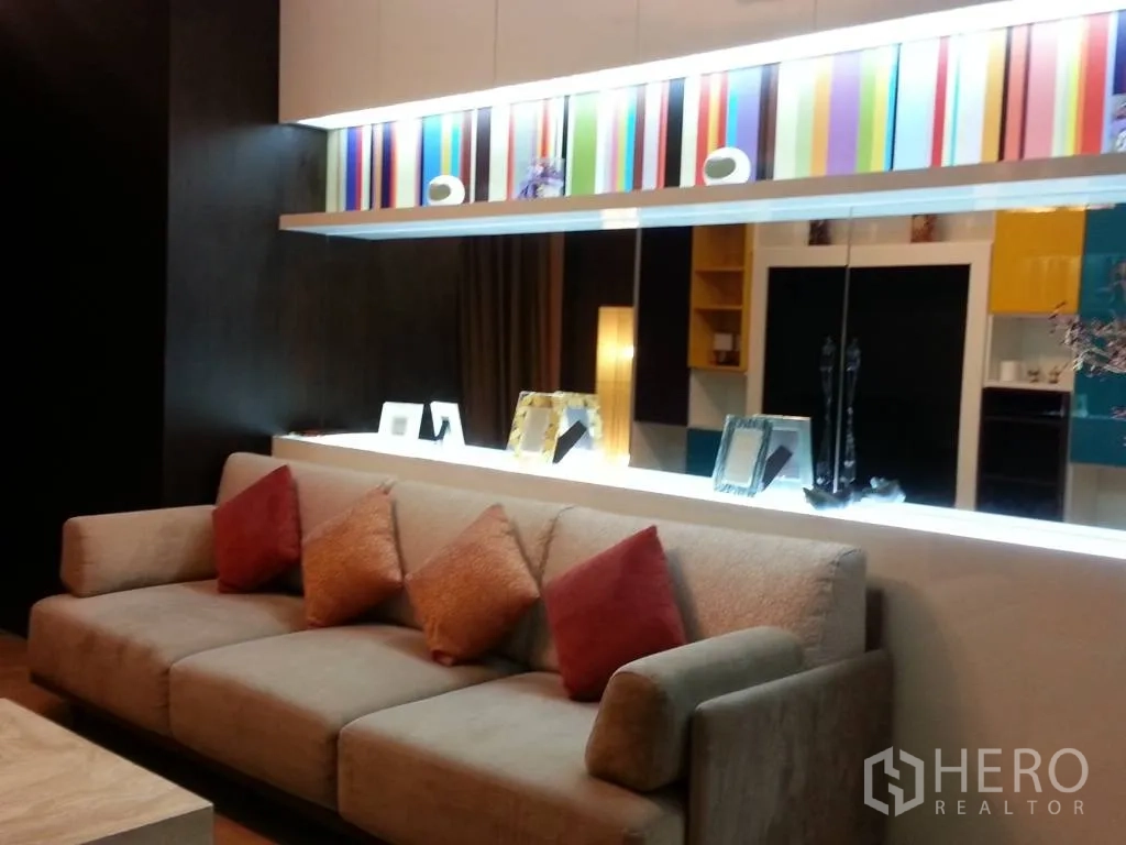 Condominium for rent in Khlong San, Bangkok - Contemporary living room with a beige sofa, colorful backlit feature wall and decorative shelving.
