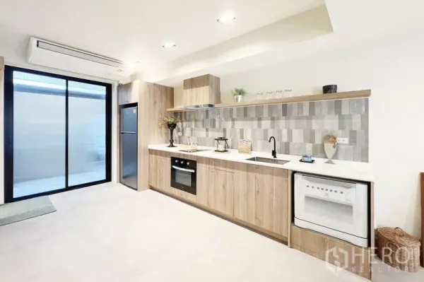 Townhouse for rent in Khlong Toei, Bangkok - Bright kitchen with light-wood cabinets, tiled backsplash, oven, fridge and sliding glass door.