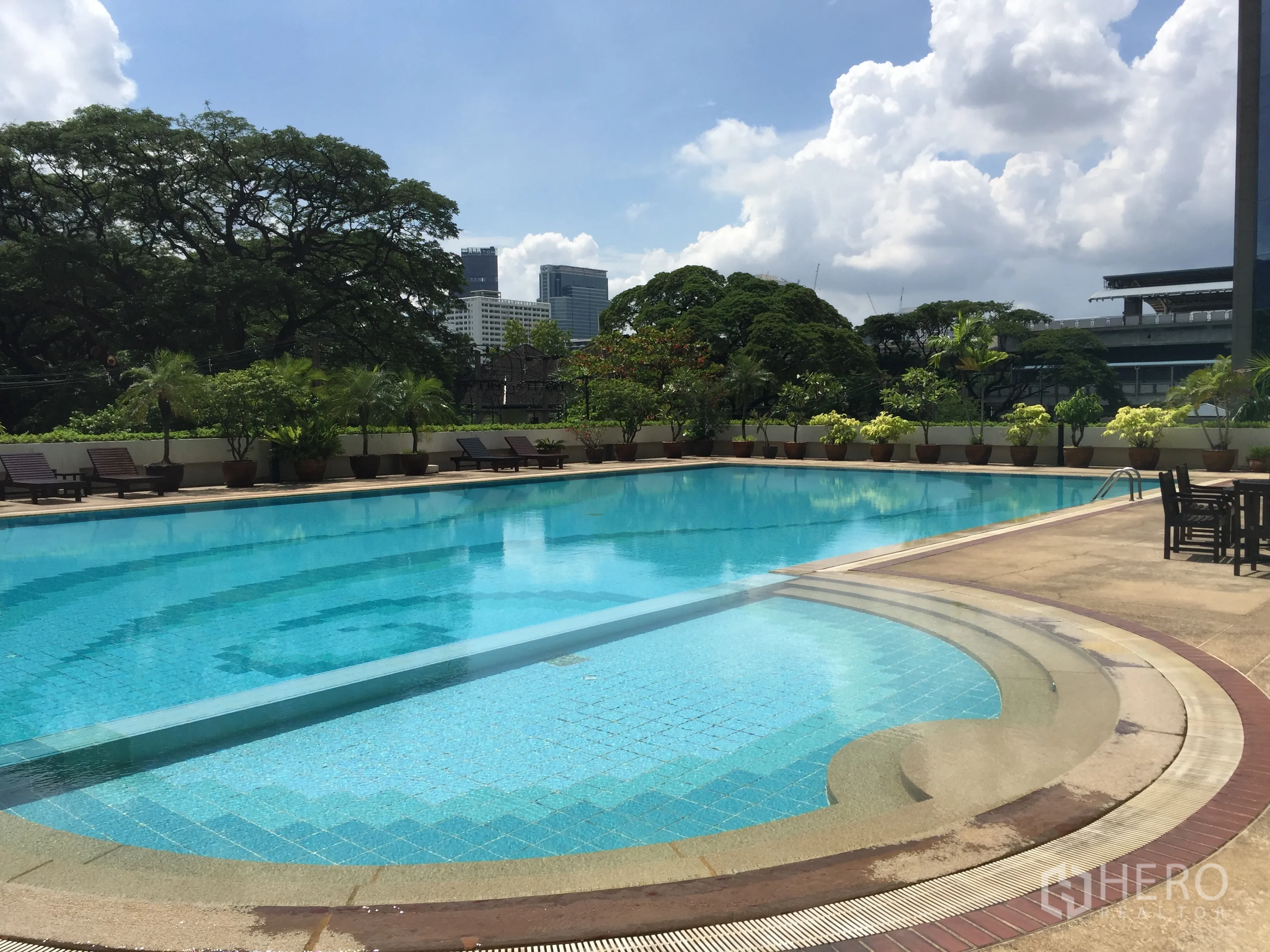 公寓 出租在Pathum Wan, Bangkok - 大型室外游泳池，设躺椅与绿化，背景为曼谷天际线。