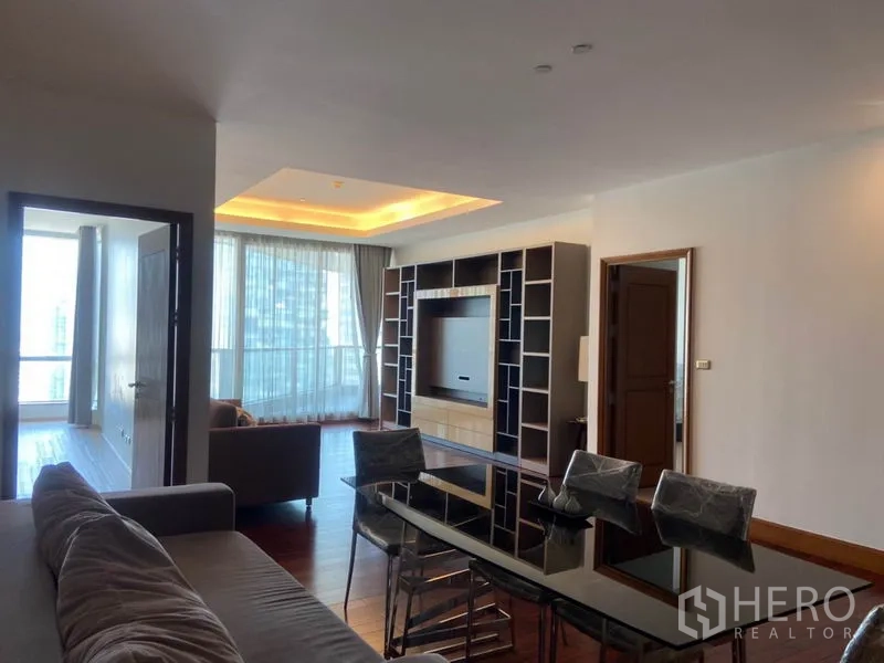 Condominium for rent in Sathon, Bangkok - Open living area with built‑in media wall, large windows, and a glass dining table.