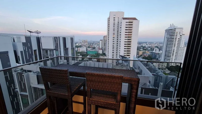 公寓 出租在Watthana, Bangkok - 高楼阳台配吧椅，俯瞰傍晚的曼谷天际线。