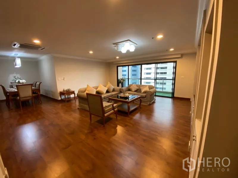 Condominium for rent in Watthana, Bangkok - Expansive living and dining area with wood floors, sofa set, and balcony overlooking nearby buildings.