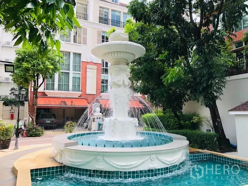 联排别墅 出租在Khlong Toei, Bangkok - 社区中庭喷泉与绿化景观，前方为低层联排建筑。