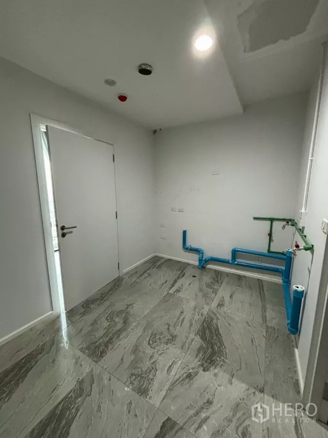 Condominium for sale in Bang Kho Laem, Bangkok - Utility room view showing blue pipes, recessed lights and grey marble-look tiles.
