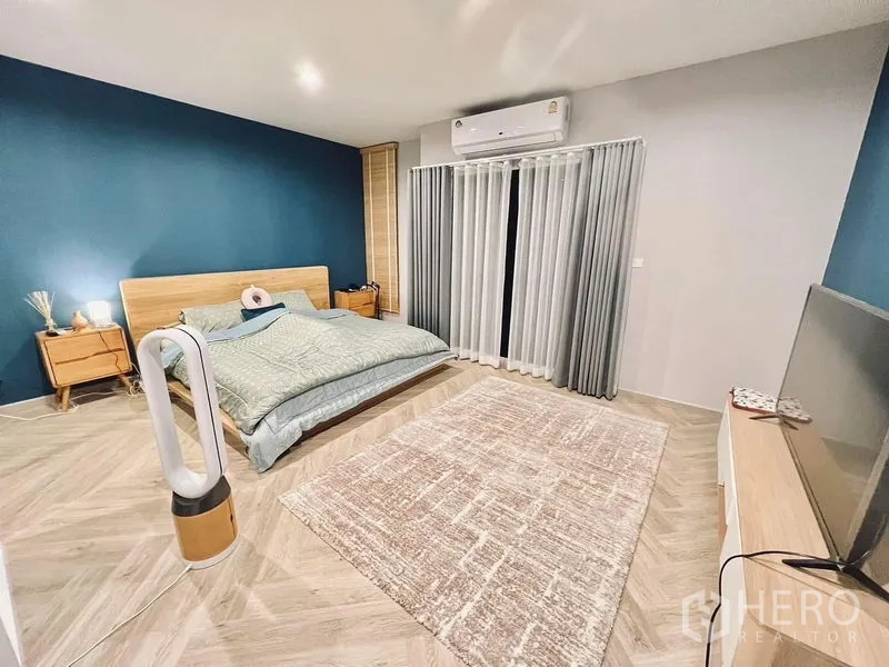 Townhouse for rent in Bang Kapi, Bangkok - Spacious master bedroom with teal accent wall, king bed, air conditioner, and sheer curtains to the balcony.
