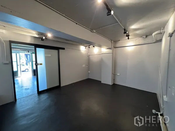 Retail Space for rent in Watthana, Bangkok - Empty interior room with track lighting, exposed ceiling conduits, grey walls and a sliding glass door to the entrance.