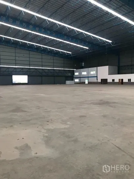 货栈 出租在Samut Prakan - 宽敞的仓库内部，高挑钢桁架屋顶，明亮LED照明与抛光混凝土地面。