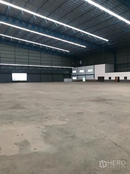 货栈 出租在Samut Prakan - 宽敞的仓库内部，高挑钢桁架屋顶，明亮LED照明与抛光混凝土地面。