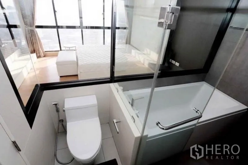 公寓 出租在Khlong San, Bangkok - 浴室内的浴缸靠玻璃隔断，可见卧室