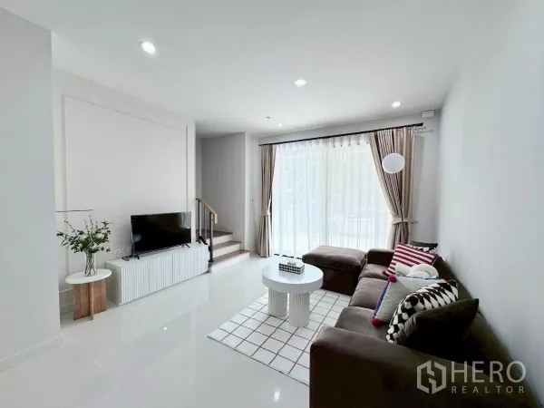 Townhouse for rent in Saphan Sung, Bangkok - Cozy living room with TV console, large windows and stairs to upper floors.