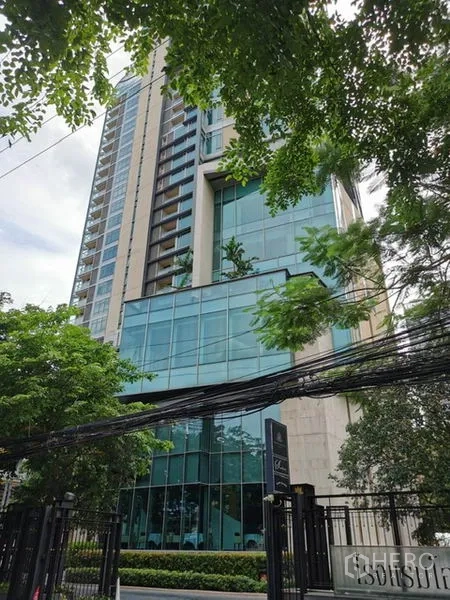 Condominium for rent in Pathum Wan, Bangkok - Modern high-rise condominium facade with glass podium and greenery.