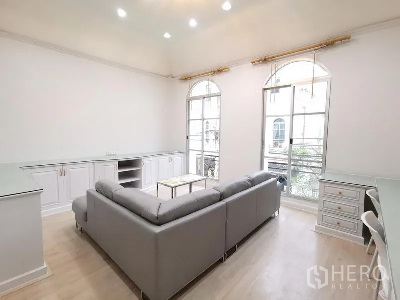 Townhouse for rent in Yan Nawa, Bangkok - Light-filled living room with gray L-shaped sofa, arched French windows and built-in cabinets.