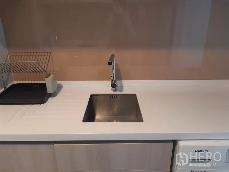 Condominium for rent in Khlong Toei, Bangkok - Modern kitchen sink with drainer and chrome faucet against a glossy backsplash.