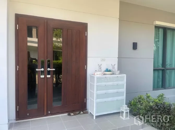 Detached House for rent or sale in Saphan Sung, Bangkok - Front entrance with solid wood double doors and a small porch cabinet.