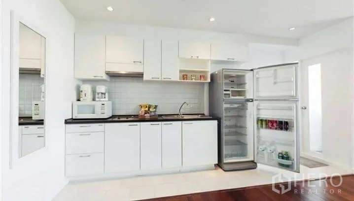 Condominium for rent or sale in Watthana, Bangkok - Compact white kitchen with cabinets, cooktop, sink and open refrigerator.