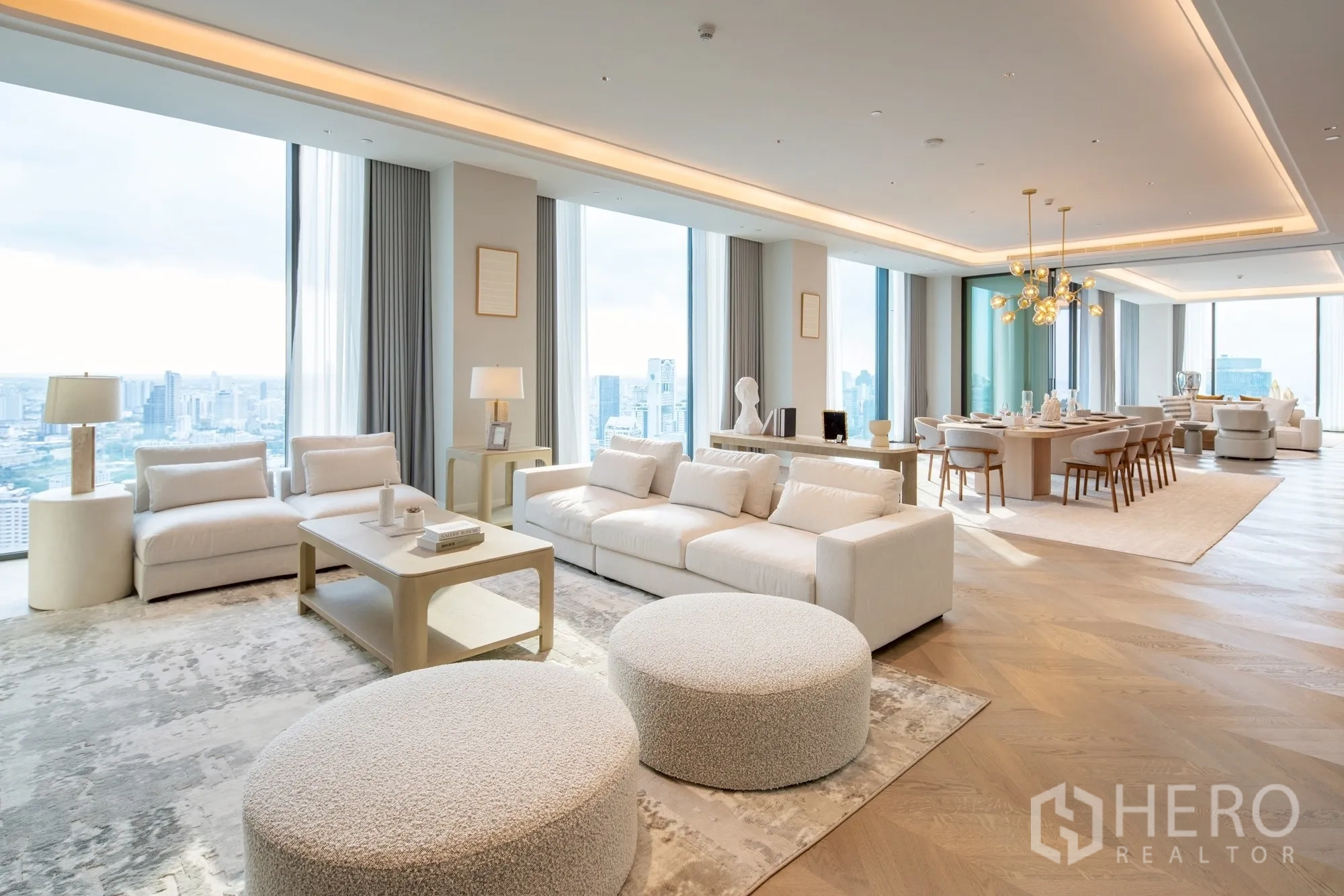 คอนโด for rent or sale in Pathum Wan, Bangkok - ห้องนั่งเล่นและรับประทานอาหารขนาดใหญ่ของเพนท์เฮาส์ กระจกสูงจรดเพดาน เฟอร์นิเจอร์โทนสว่าง โคมไฟแชนเดอเลียร์ และวิวเมืองกว้าง