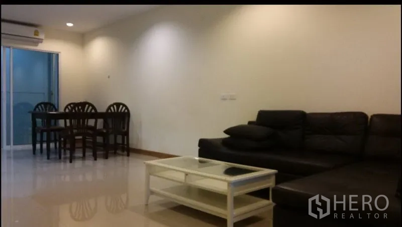 Townhouse for rent in Suan Luang, Bangkok - Open-plan lounge with L-shaped sofa, coffee table, and dining corner under recessed lighting.