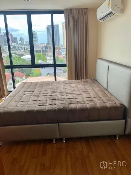Condominium for rent in Watthana, Bangkok - Bedroom with large window, city view and air conditioner in a Watthana condominium.